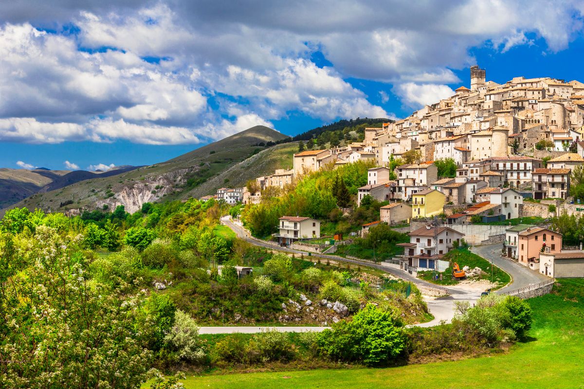 Castel del Monte - Abruzzo Panoramautsikt over den historiske landsbyen Castel del Monte i Abruzzo, omgitt av grønne åser og majestetiske fjell i bakgrunnen.
