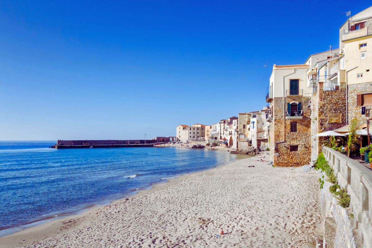 Stranden i Cefalù – en av Sicilias vakreste småbyer, med gyllen sand, klart vann og historiske hus rett ved sjøen.