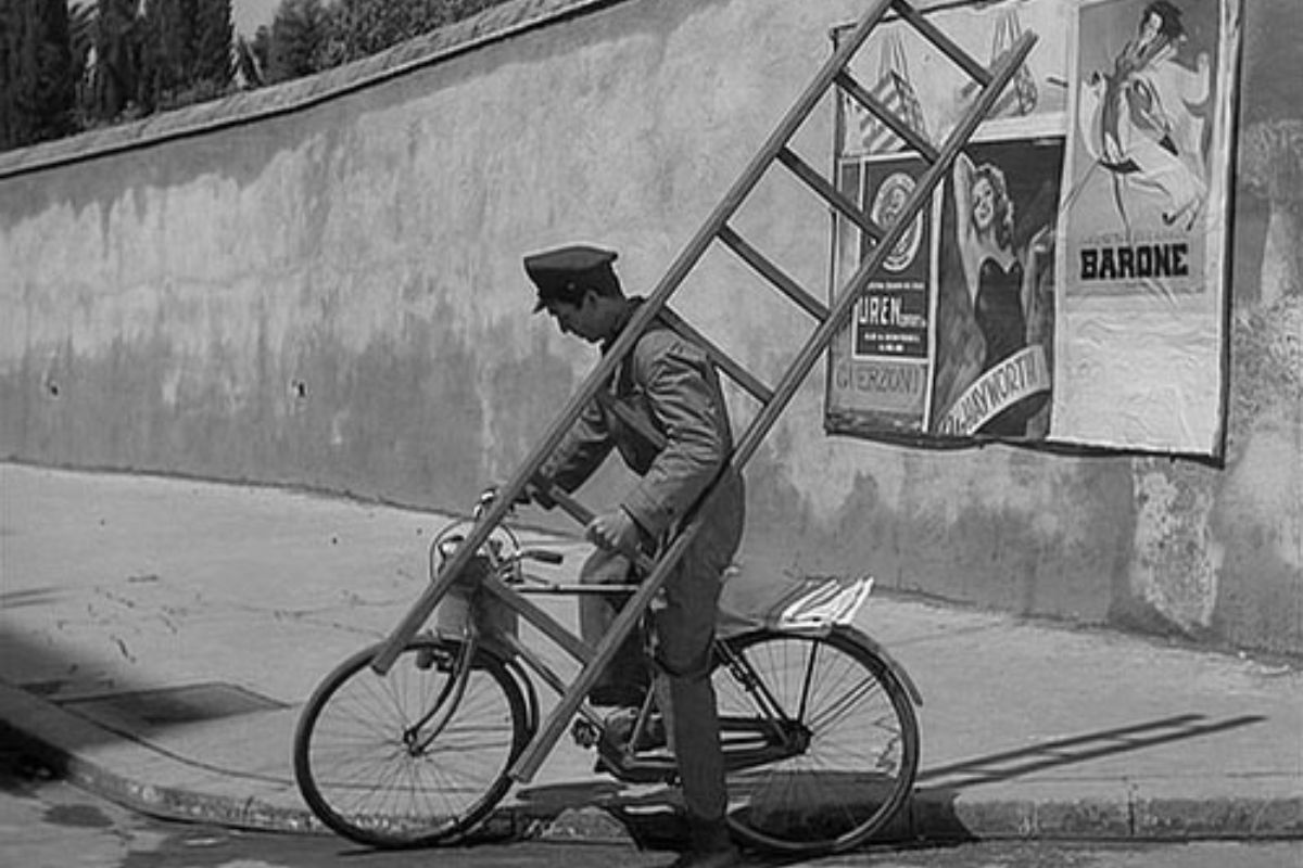 Antonio henger opp plakater med sykkelen – fra filmen Ladri di biciclette