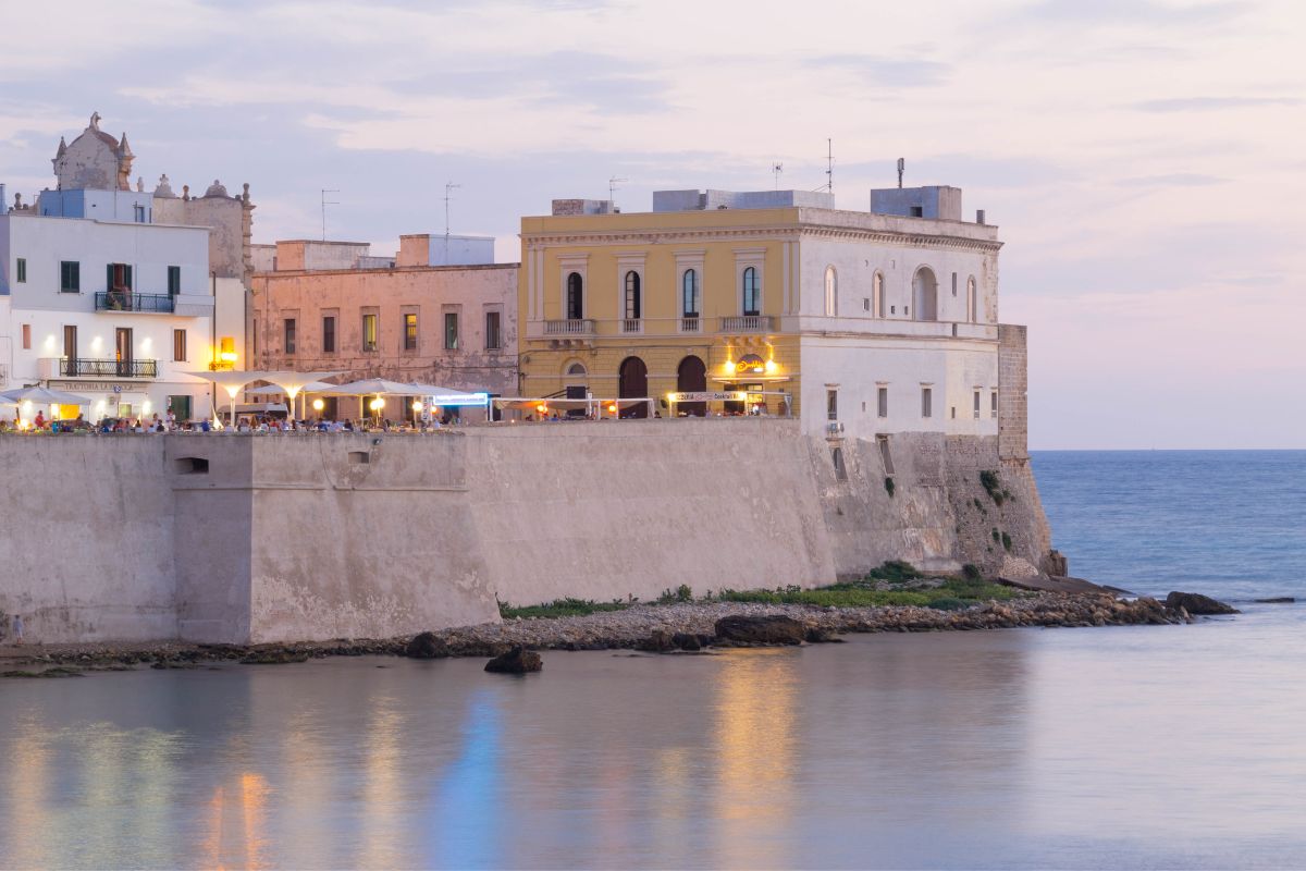 Gamlebyen i Gallipoli ved solnedgang, med historiske bygninger og restauranter langs sjøen i Puglia, Italia.