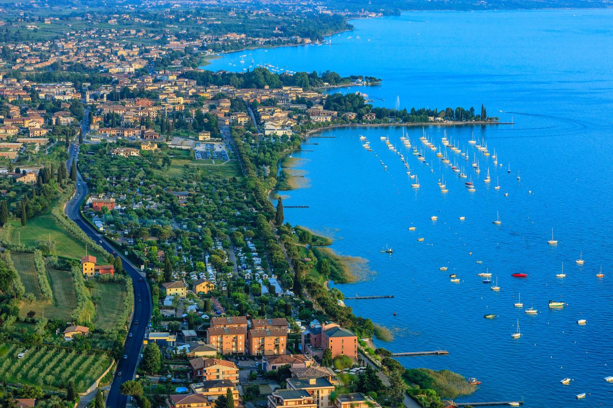 Gardasjøen3 Gardasjøen – panoramautsikt over kysten med båthavn, strender og grønt landskap i Veneto.