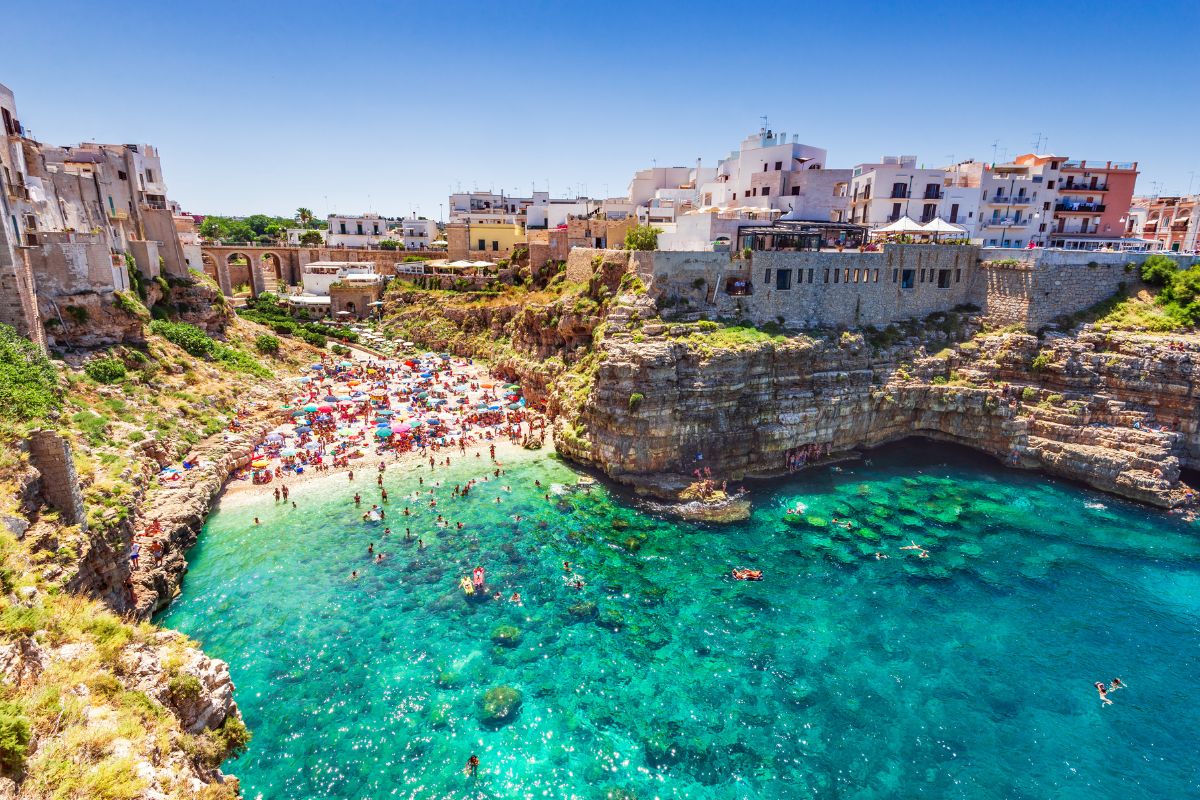 Folksom strand med klipper og turkist vann i Polignano a Mare, en av de mest kjente kystbyene i Puglia.