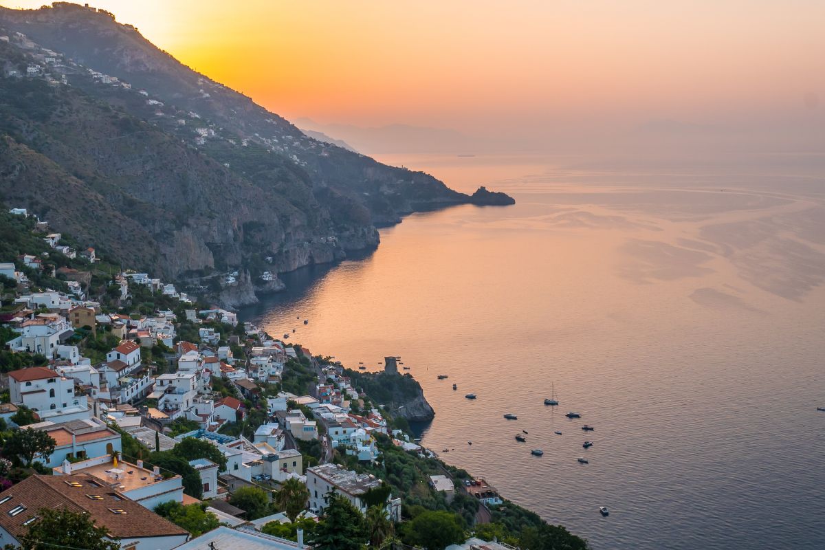 Praiano i solnedgang med hvite hus og båter langs kysten