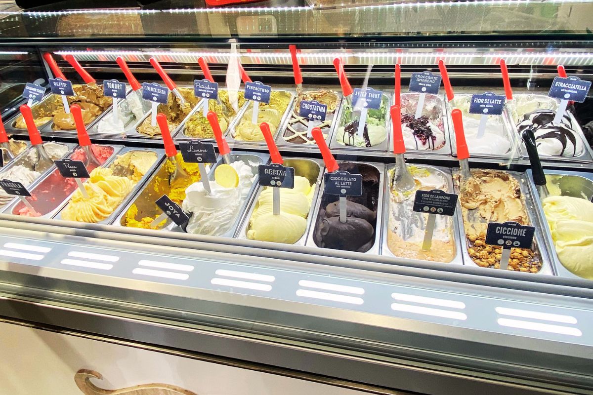 Utvalg av italiensk gelato i en tradisjonell iskrembar: klassiske smaker som pistasj, sjokolade og sitron, og kreative navn som “Ciccione” og “Joya”.