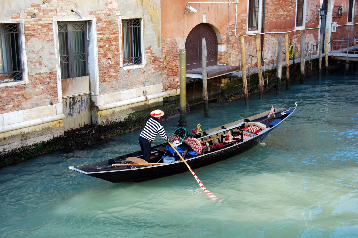 Gondola Gondolier i Venezia som ror en gondol på en smal kanal foran gamle husfasader.