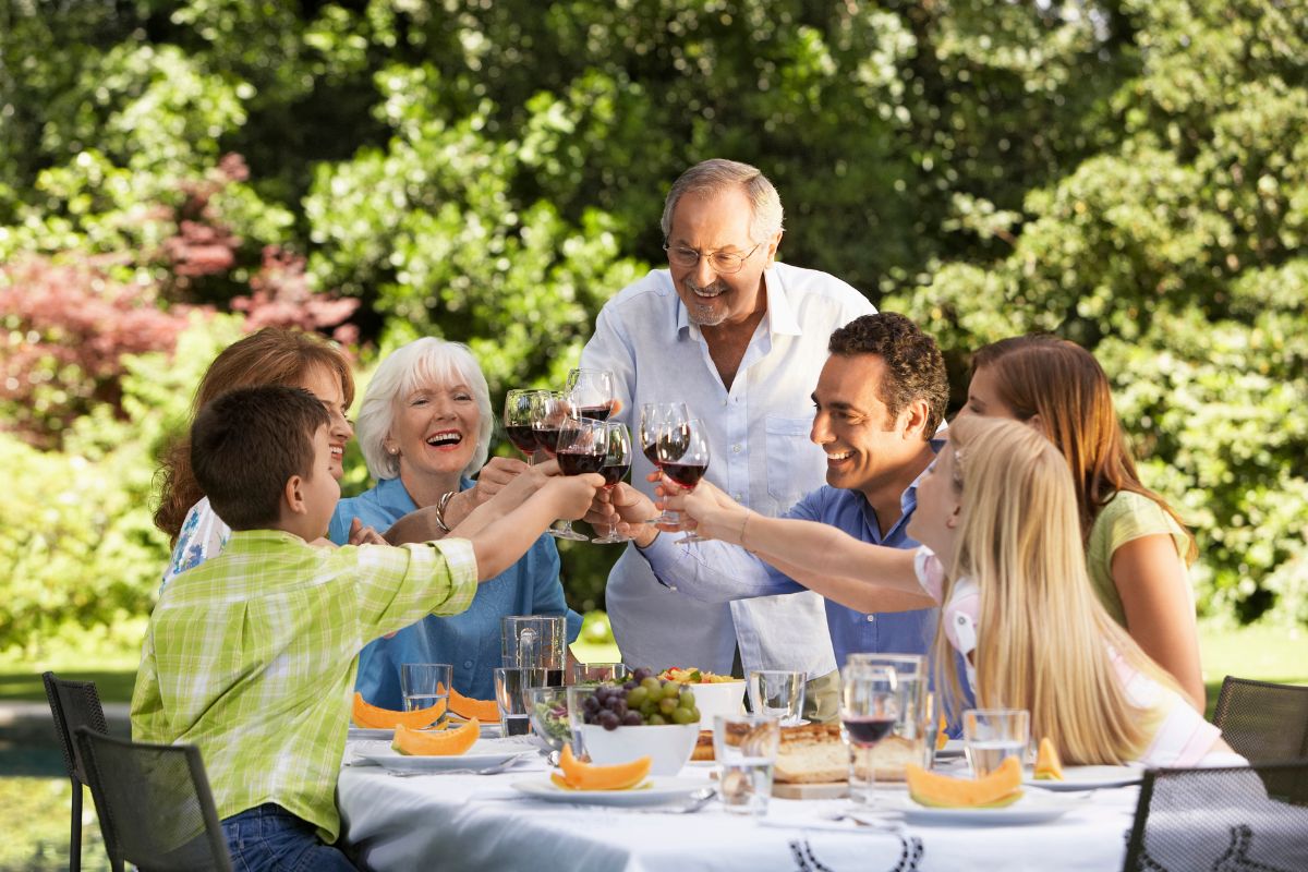 Familie og venner som skåler rundt et utendørs sommerbord med vin og mat i hagen.