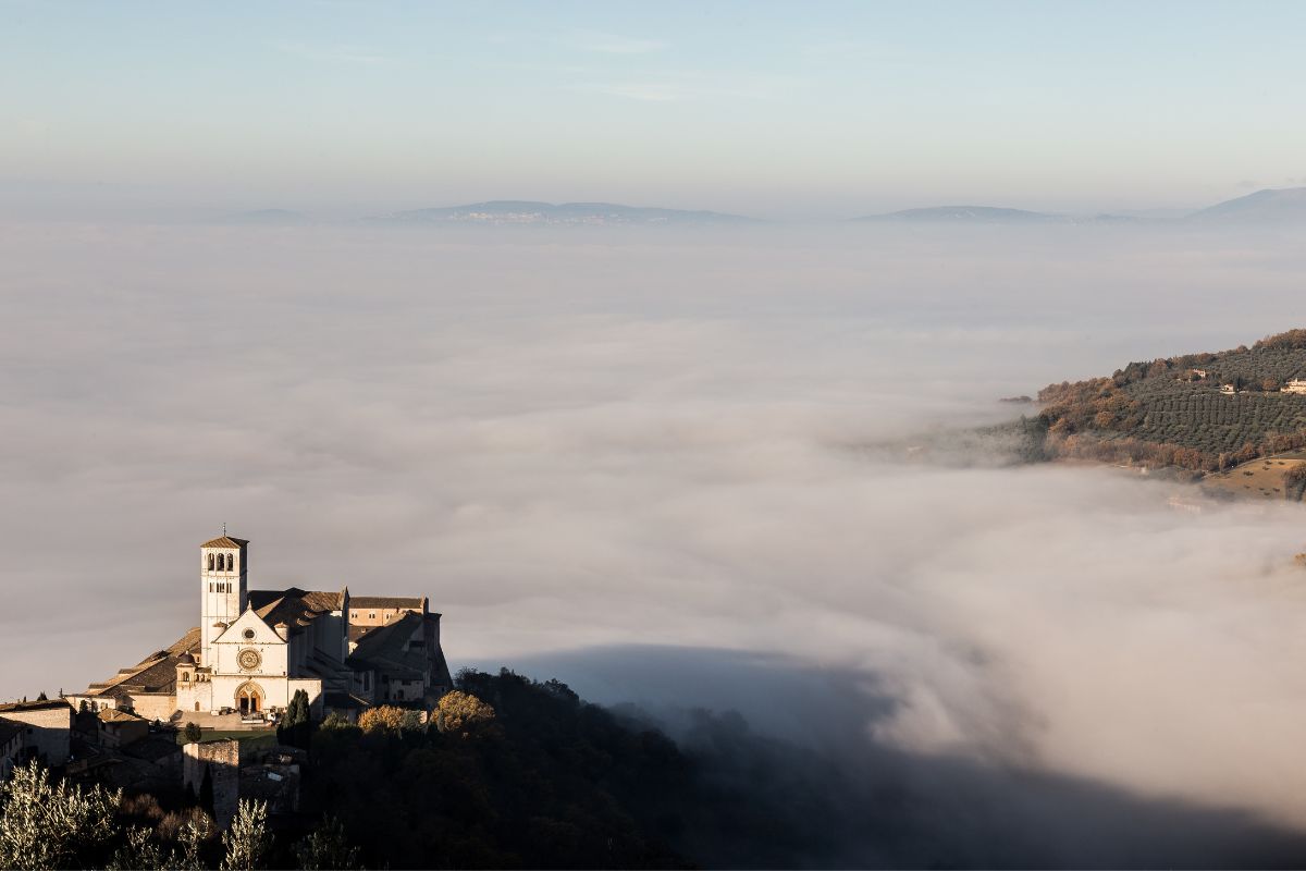 Paradishøyden-Assisi Basilica di San Francesco i Assisi stiger opp over tåkehavet på Paradishøyden, med fjellene som skimtes i horisonten.