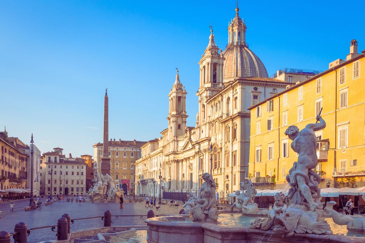 Piazza Navona i Roma, med barokke fontener, obelisk og kirken Sant’Agnese in Agone under en klar, blå himmel.