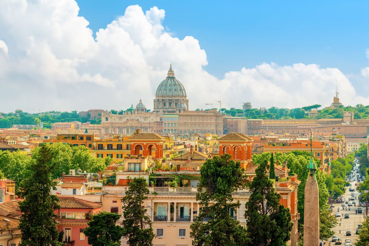 Panoramautsikt over Roma på en solrik dag, med Peterskirken og byens fargerike bygninger i forgrunnen.