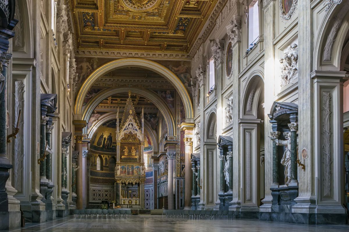Midtskipet i San Giovanni in Laterano i Roma, med kraftige søyler, monumentale apostelstatuer og det gotiske baldakinet over høyalteret.