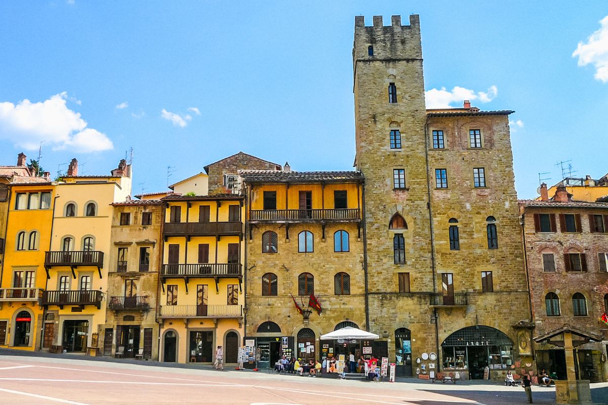 Tom piazza i Arezzo med historiske bygninger og få mennesker under en klar blå sommerhimmel.