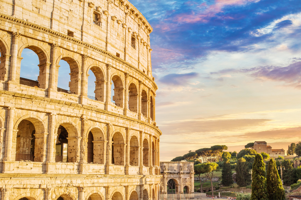 Colosseum i Roma ved solnedgang, med utsikt mot Konstantinsbuen og pinjetrær i bakgrunnen.