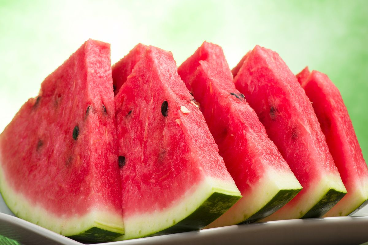 Saftige skiver av rød vannmelon med mørke frø, arrangert på et fat, mot en grønn og lys bakgrunn.