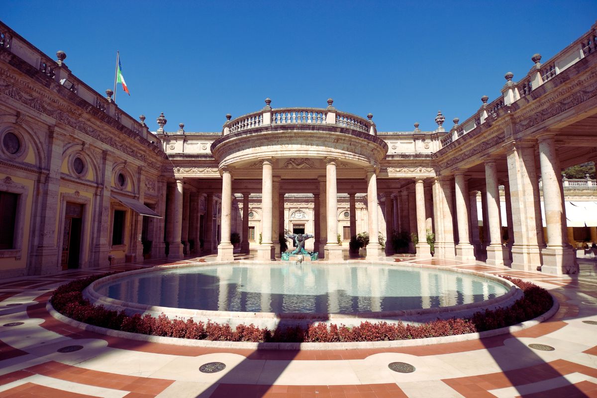 Historisk spa-anlegg i Montecatini Terme, Toscana – klassisk bygning i jugendstil med søylegang og rund fontene under blå himmel.