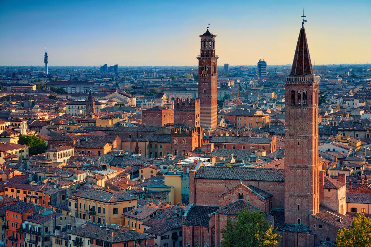 Panoramautsikt over Verona med middelaldertårn og kirker, som viser byens historiske skyline i kveldssolen.