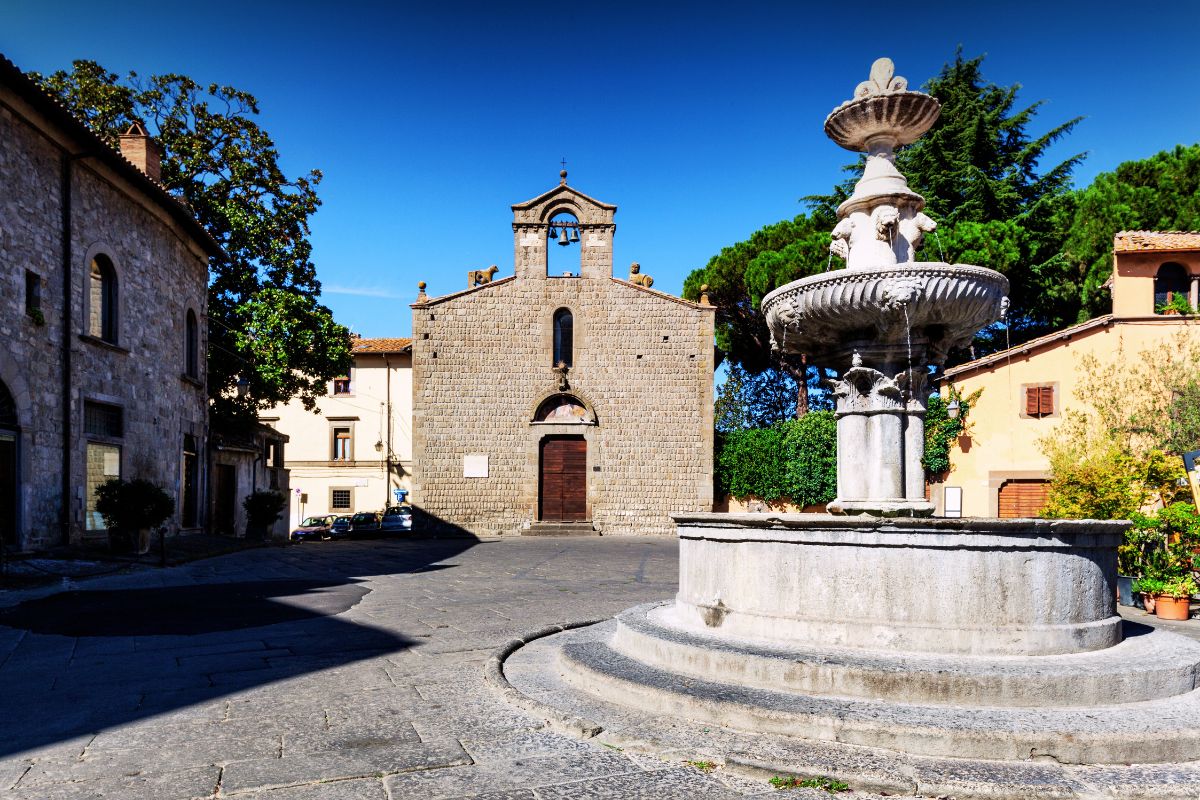 Historisk torg i Viterbo (Lazio) med en steinkirke i romansk stil i bakgrunnen og en dekorativ fontene i forgrunnen.
