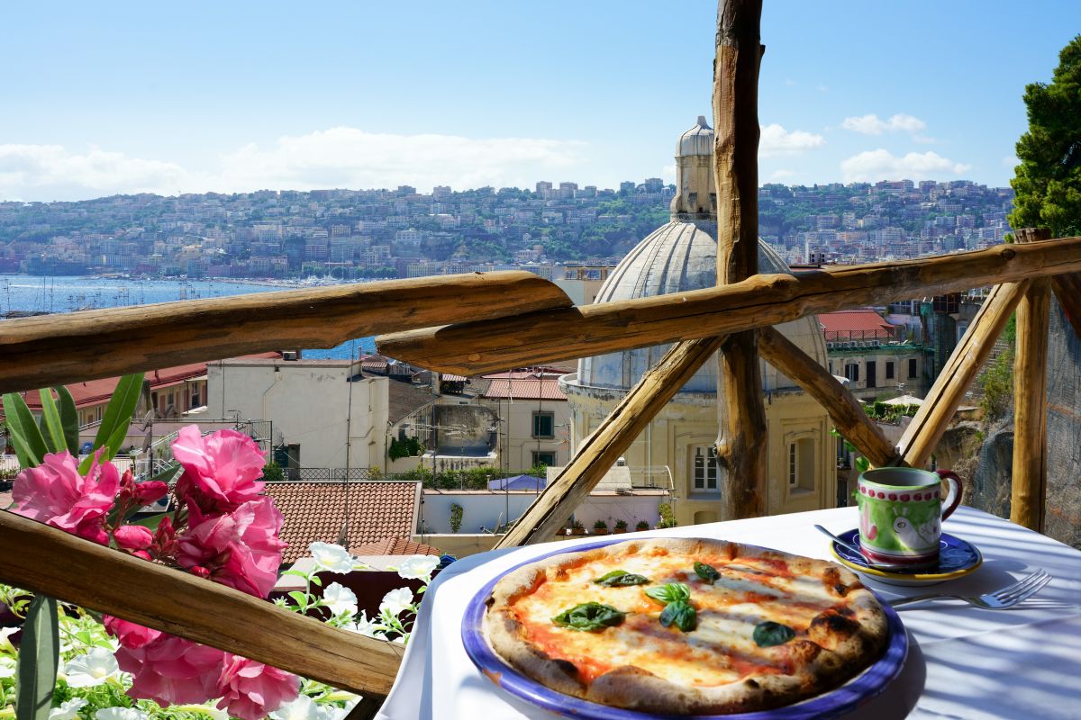 Pizza margherita og kaffe på et bord med utsikt over Napoli og Napolibukta – et perfekt bilde av napolitansk livsglede.