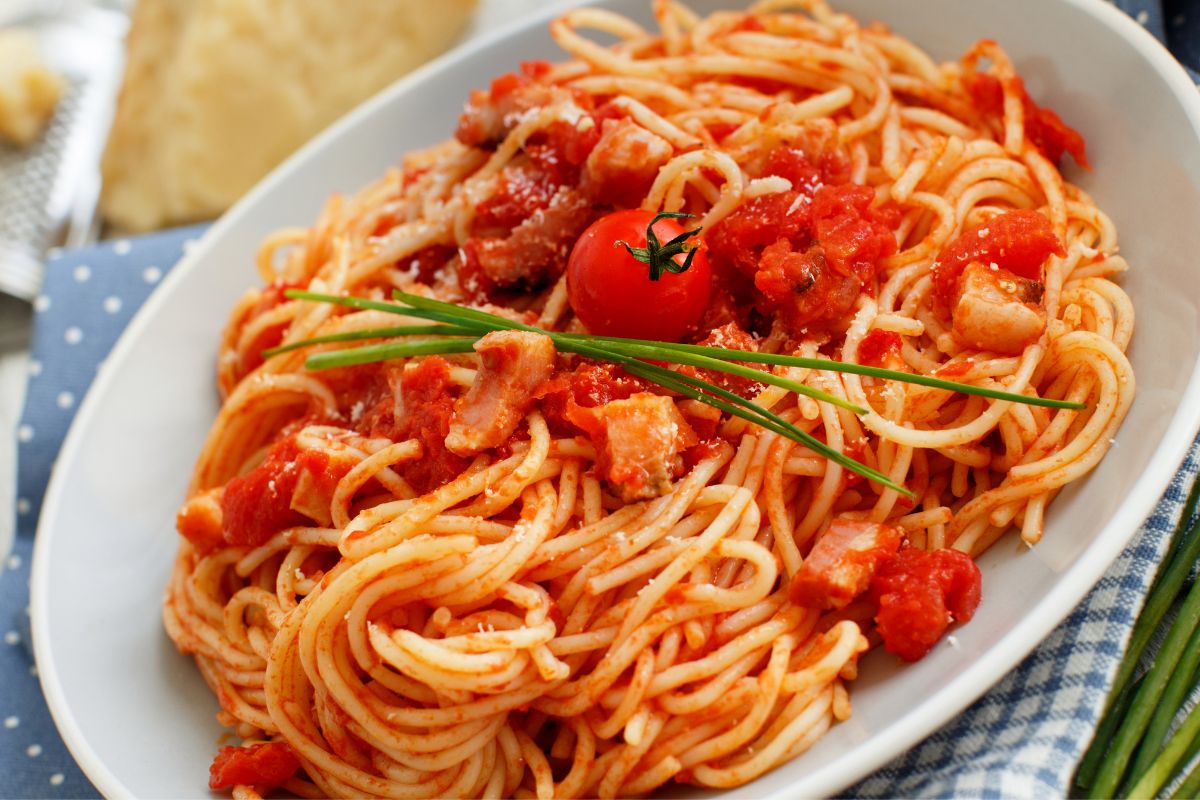 En tallerken med spaghetti all’amatriciana – klassisk italiensk pasta med tomatsaus, sprø guanciale og revet pecorino, pyntet med et lite tomat og gressløk.