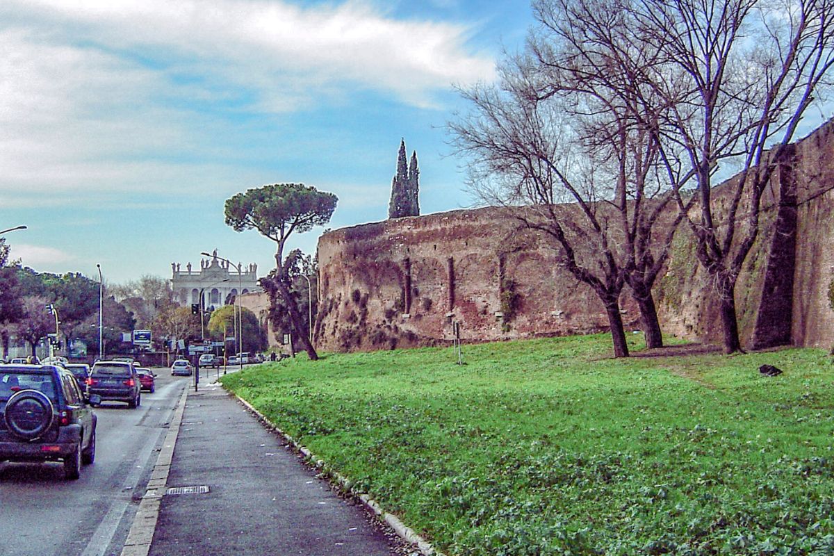 Amfiteateret Castrense som en del av Aurelianmuren i Roma, sett fra veien med trafikk på venstre side og grøntområde og trær foran murveggen.