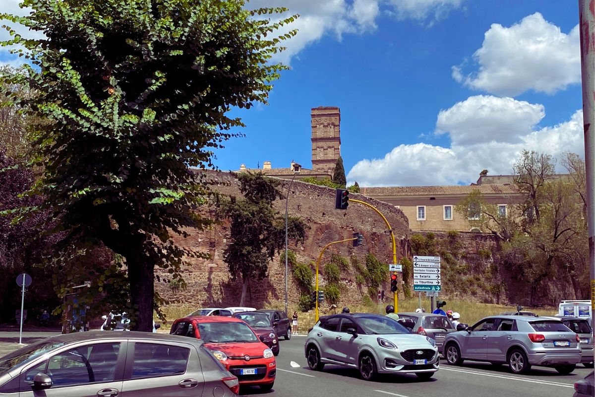 Amfiteateret Castrense og Aurelianmuren sett fra en trafikkert vei i Roma, med biler, lyskryss og bygninger i bakgrunnen.