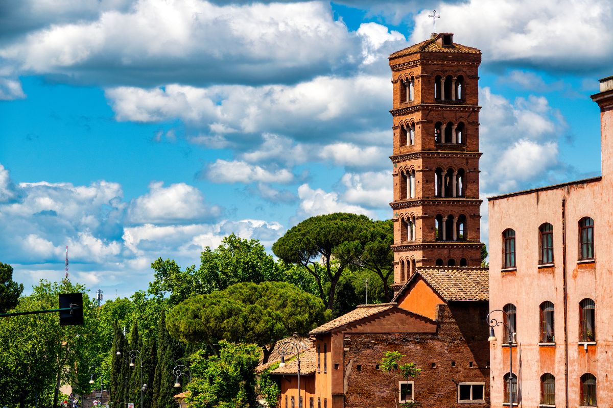 Det romanske klokketårnet til Santa Maria in Cosmedin i Roma, omgitt av trær og bygninger under en blå himmel