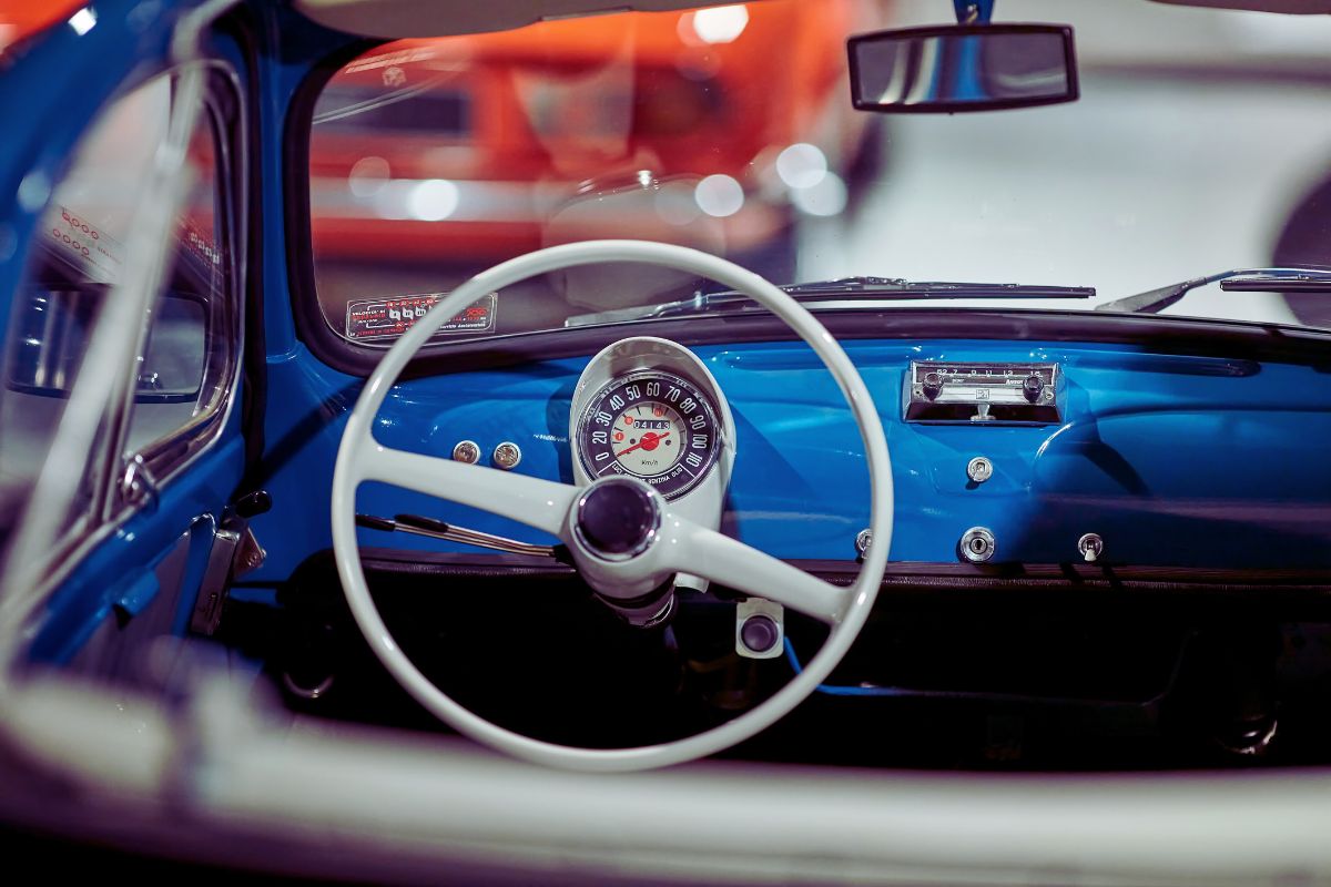 Interiør av en vintage Fiat 500, med blått dashbord, hvitt ratt og det karakteristiske runde speedometeret.