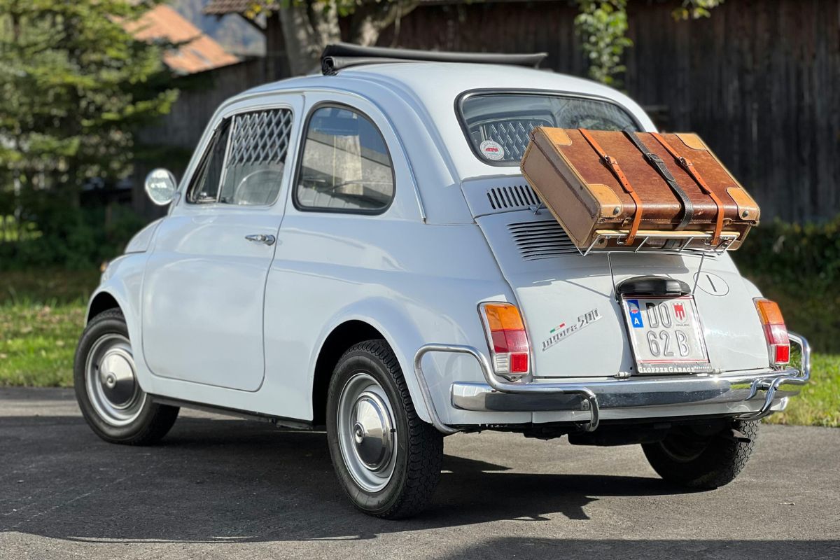 Hvit Fiat 500 fra 60-tallet med gammel brun koffert festet på bagasjestativet.