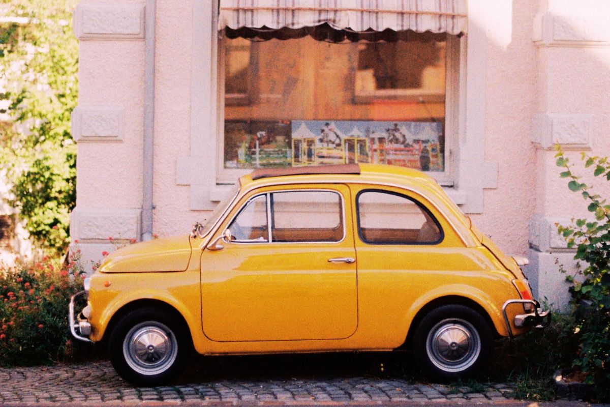 Gul klassisk Fiat 500 parkert foran et gammelt hus – et ikonisk symbol på italiensk design og 60-tallets Italia.