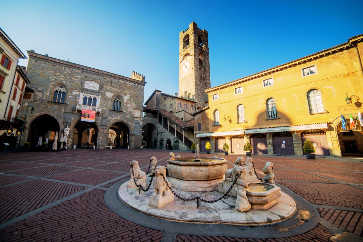 Piazza Vecchia i Bergamo med fontenen, Palazzo della Ragione og Campanone i bakgrunnen, tidlig morgenlys i Città Alta.