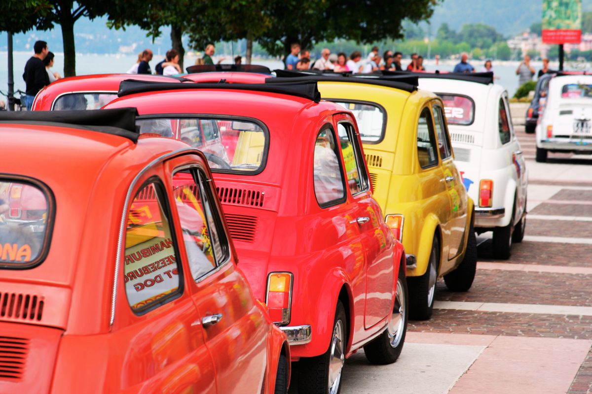 Fargerike Fiat 500 på rekke under et treff for entusiaster ved en italiensk innsjø.