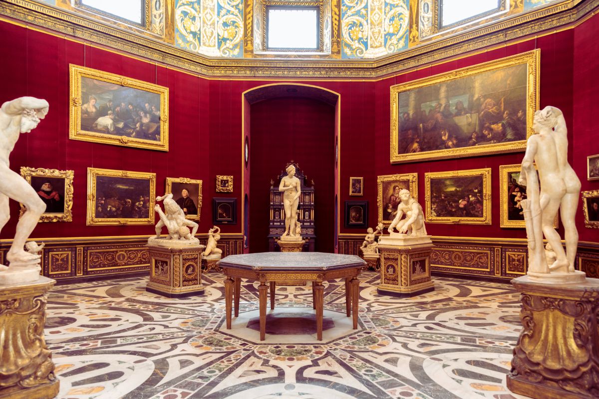 Interiør fra Uffizi-galleriet i Firenze med rødvegger, marmorskulpturer og malerier fra renessansen.