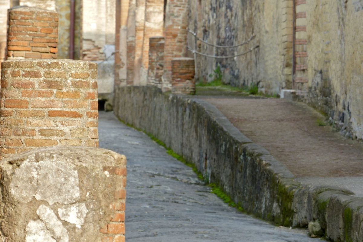 Detalj av antikk gate i Herculaneum med steinlagt vei, murvegger og godt bevarte romerske strukturer.