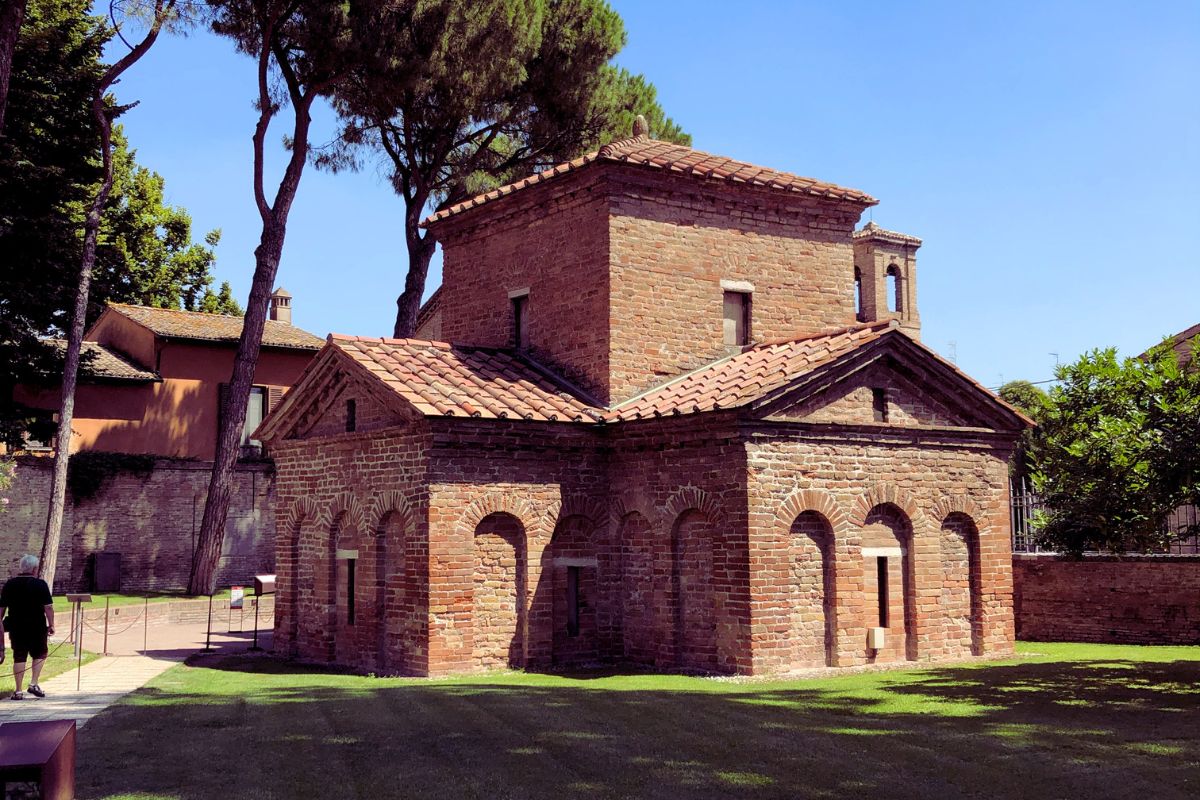 Galla Placidia-mausoleet i Ravenna sett utenfra, en liten mursteinsbygning fra tidlig kristen tid omgitt av trær og grøntområde.