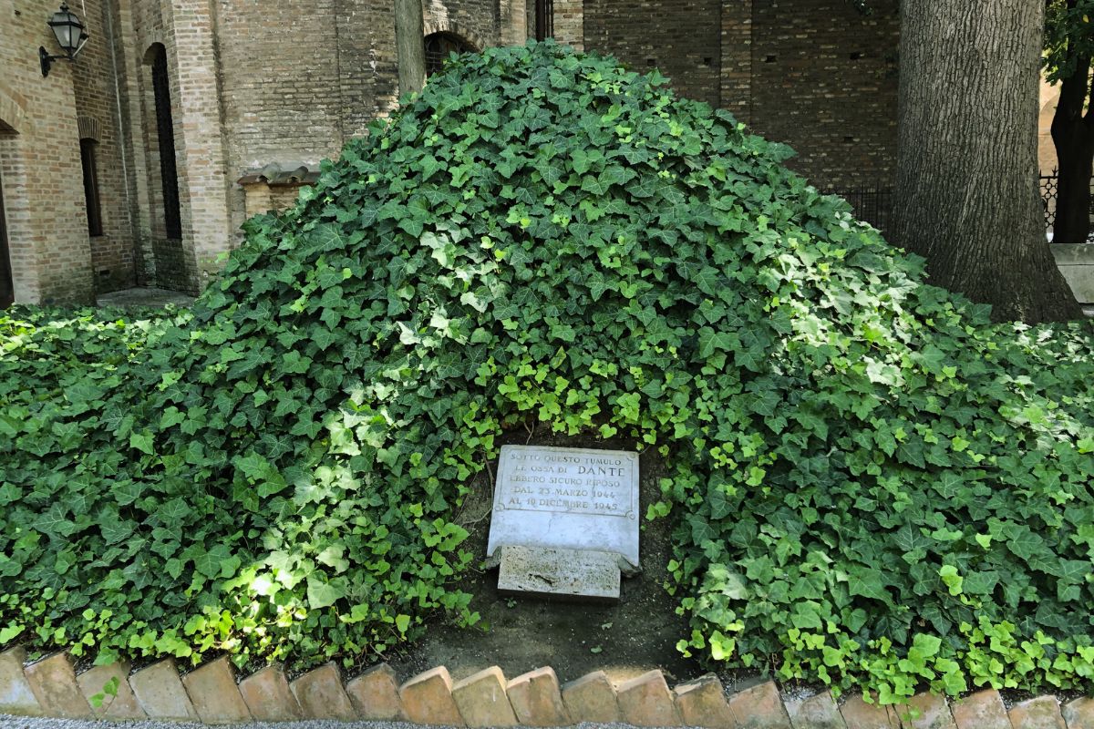 Dantes grav i Ravenna, delvis dekket av grønne planter, med en enkel minnestein foran.