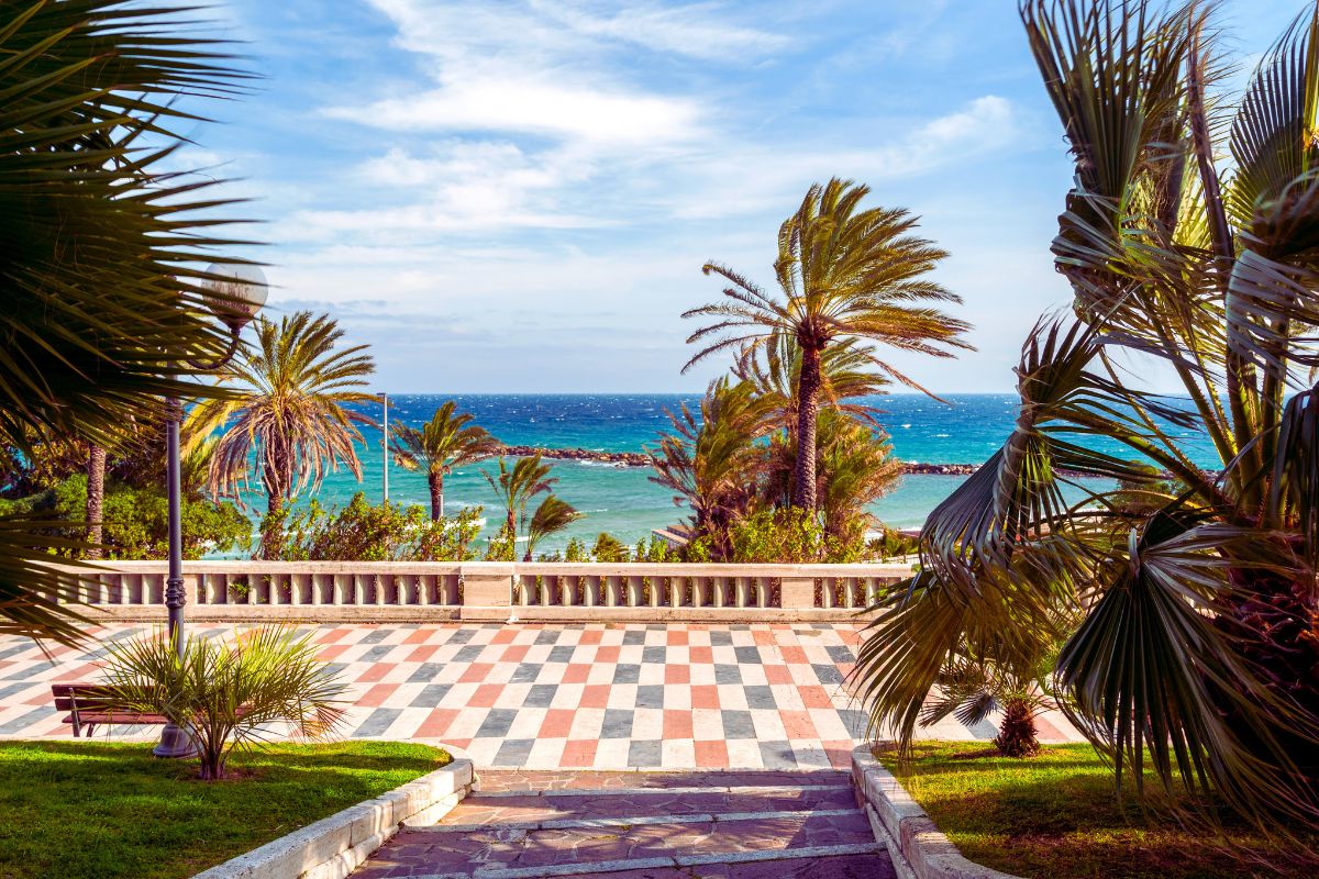 Palmer langs strandpromenaden i Sanremo med utsikt over det blå Middelhavet. Den elegante kystbyen er kjent for sitt milde klima, sine hager og sin vakre beliggenhet på den italienske rivieraen.
