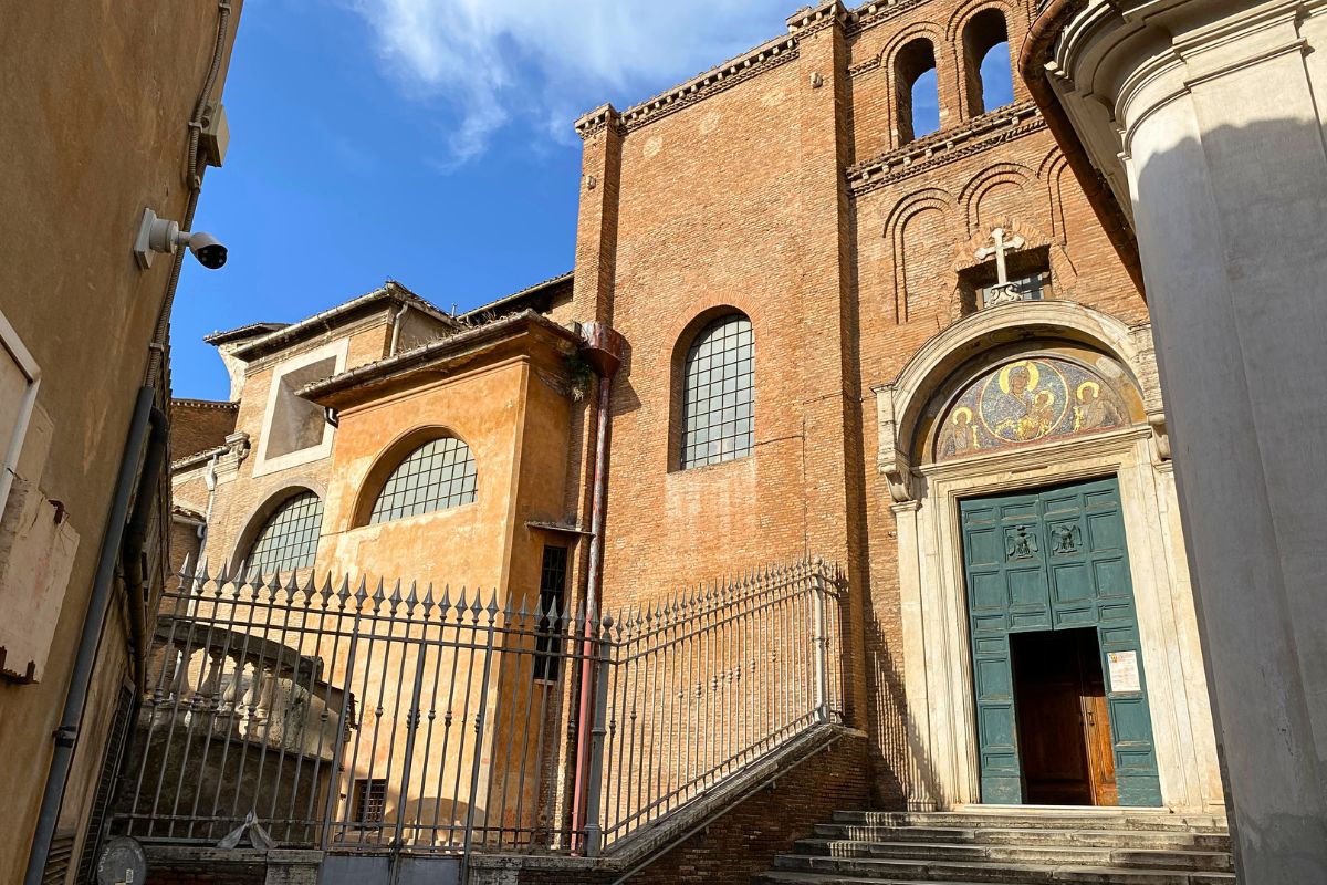 Sideinngangen til Santa Maria in Aracoeli i Roma. Den enkle mursteinsfasaden viser basilikaens middelalderske opprinnelse, mens mosaikken over portalen minner om kirkens lange religiøse tradisjon. Bygningen ligger på Kapitolhøyden og skiller seg ut fra mange av Romas mer praktfulle kirker med sitt nøkterne og historiske uttrykk.